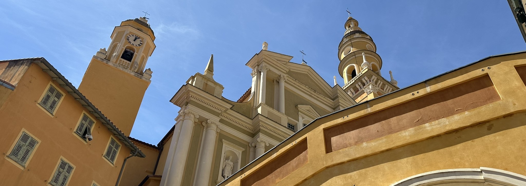 Close-up of the ornate facade and bell towers of Basilique Saint-Michel-Archange in Menton, France, under a clear blue Riviera sky