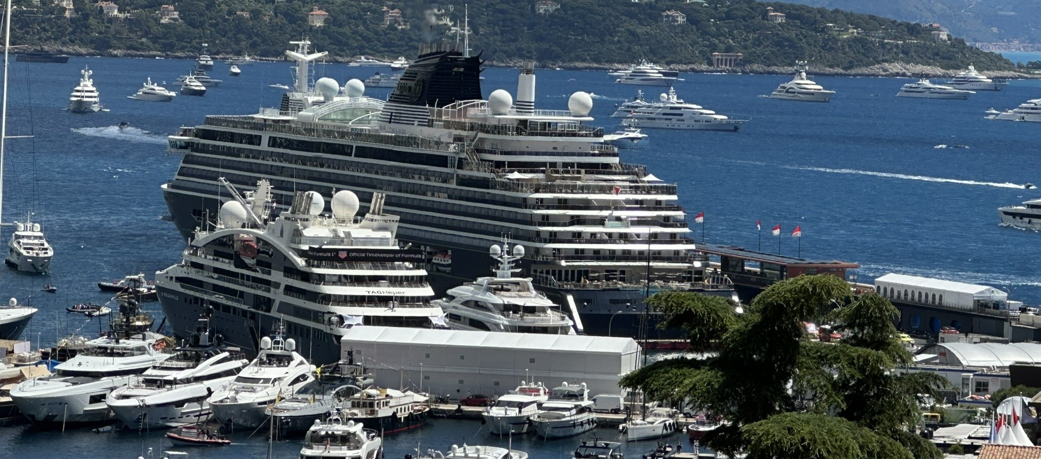 Scenic view of Port Hercules in Monaco with luxury yachts docked beneath a clear blue sky and the Mediterranean Sea beyond.